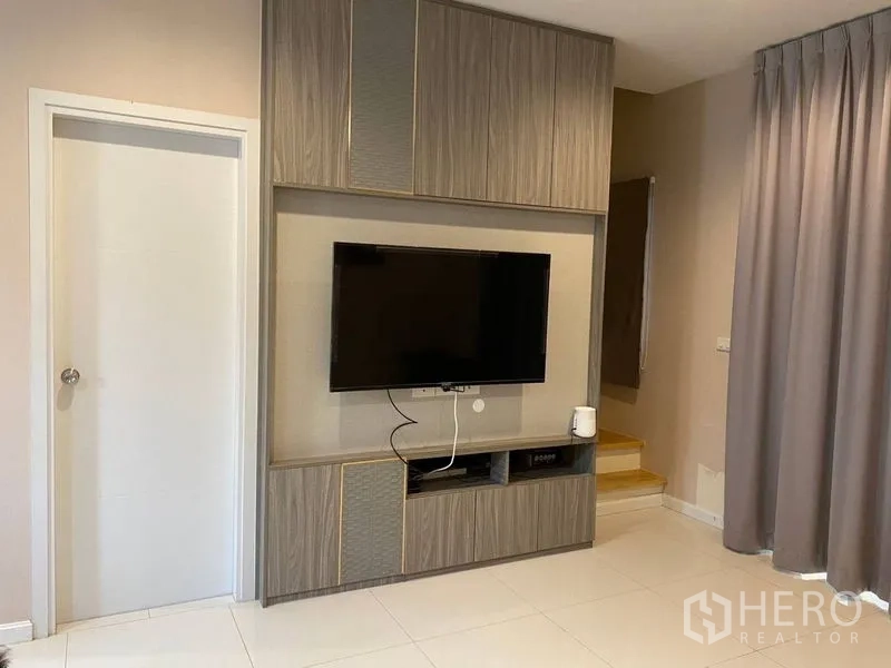 Townhouse for rent - Living room featuring a built-in media wall with mounted TV beside the staircase and grey drapes.