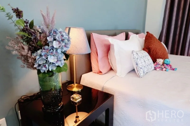 Townhouse for rent in Khlong Toei, Bangkok - Bedside vignette with lamp and floral arrangement next to a cushioned headboard.