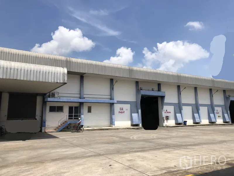 Warehouse for rent in Phra Nakhon Si Ayutthaya - Large warehouse exterior with covered loading bays and a wide truck yard under a blue sky.