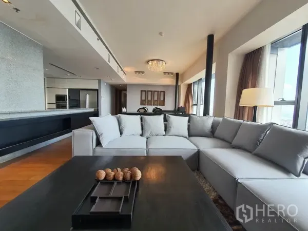 Condominium for rent in Sathon, Bangkok - Open-plan lounge with large sofa facing the kitchen counter and bright windows.