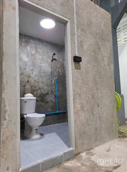 Warehouse for rent in Rat Burana, Bangkok - Warehouse restroom with toilet and shower inside a concrete-finish enclosure.