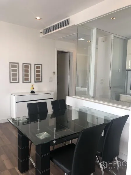 Condominium for rent or sale in Phra Khanong, Bangkok - Dining corner featuring a glass table with four black chairs and a mirrored wall over wood flooring.