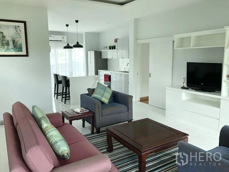 Detached House for rent or sale in Huai Khwang, Bangkok - Cozy living room with sofas, TV built-ins and large windows beside the kitchen.