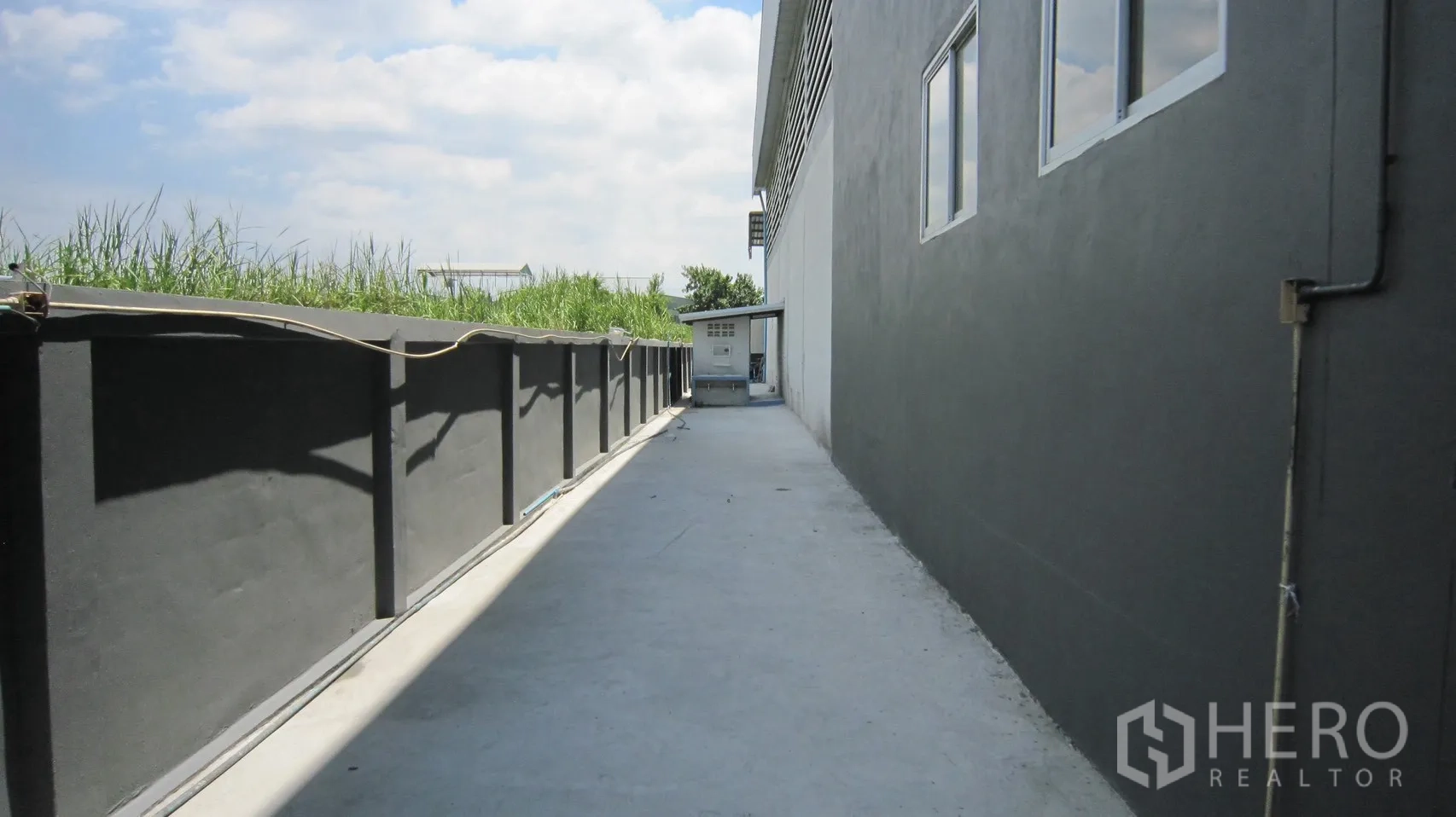 Warehouse for rent in Bang Sao Thong, Samut Prakan - Concrete side driveway beside the warehouse with perimeter wall and utility box.