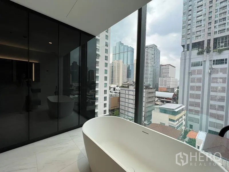 Condominium for rent in Bang Rak, Bangkok - Freestanding bathtub set by a window with high-rise city views.
