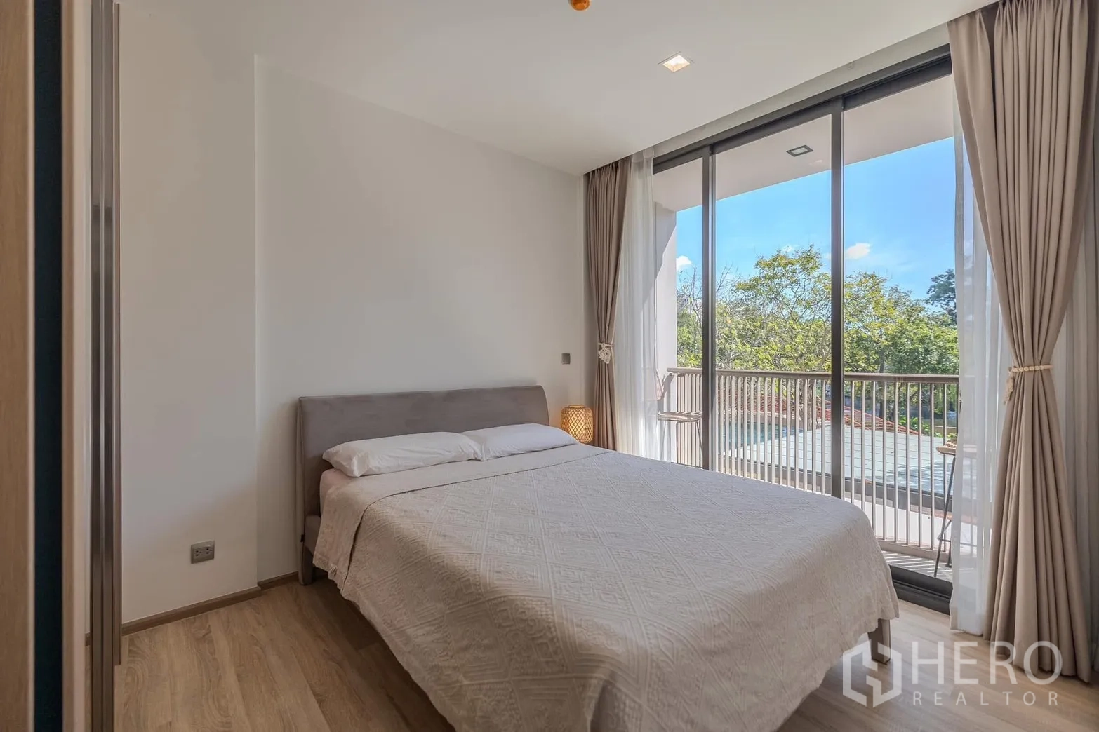 Condominium for rent in Watthana, Bangkok - Bright bedroom with double bed and floor-to-ceiling windows opening to a balcony with greenery and pool views.