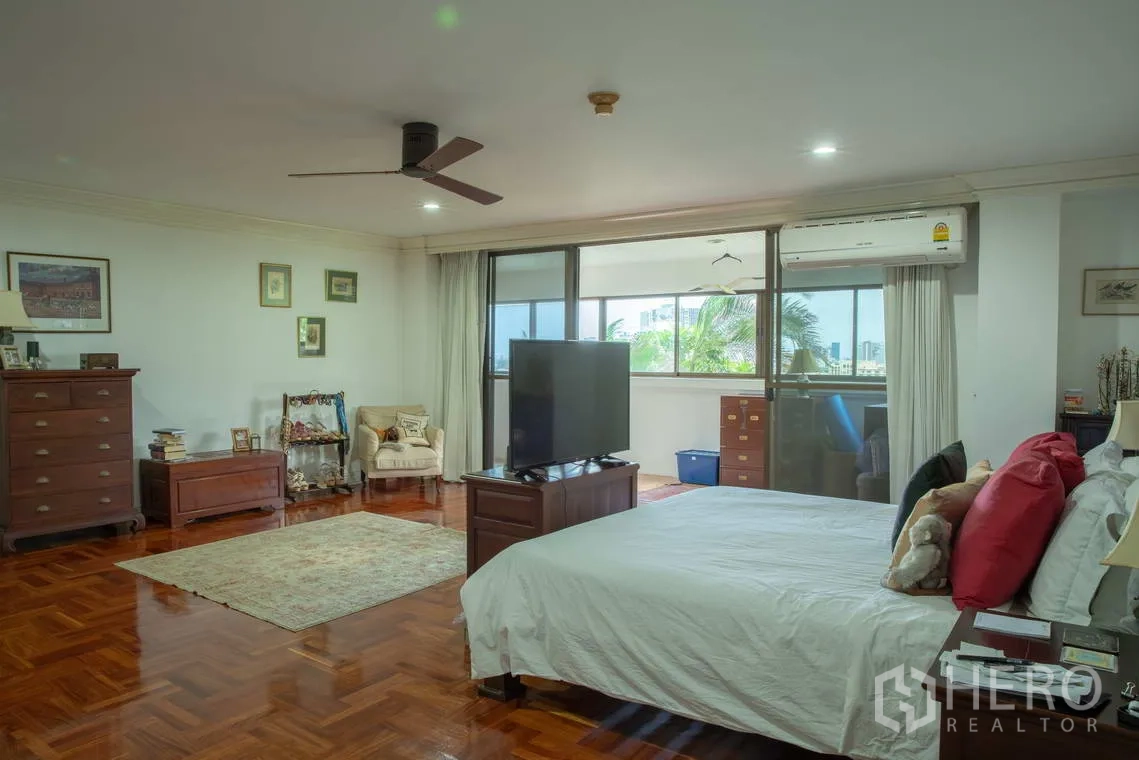 Apartment for rent in Khlong Toei, Bangkok - Spacious master bedroom with parquet floor, ceiling fan, and balcony windows.