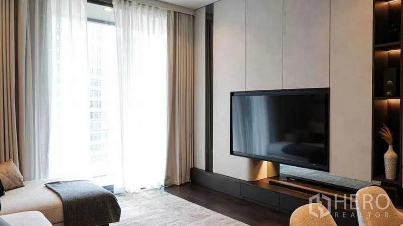 Condominium for rent or sale in Watthana, Bangkok - Living area with large TV mounted on feature wall and full-height windows.