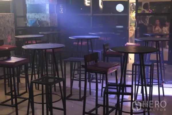 零售空间 出租在Watthana, Bangkok - 氛围灯光下的休闲区，高圆桌与吧凳，临近落地窗。
