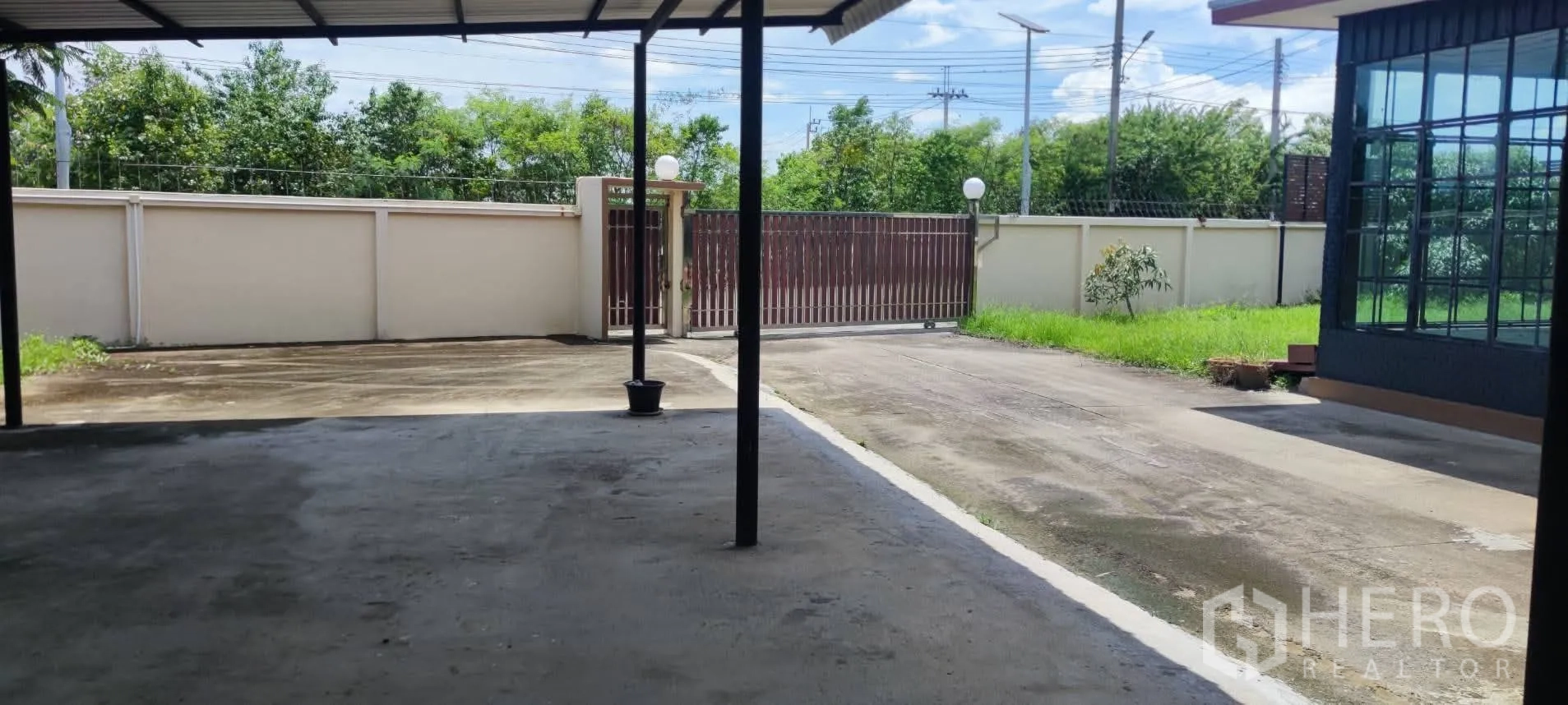 Warehouse for sale in Thung Khru, Bangkok - Covered parking area and driveway opening to sliding gate and lawn.