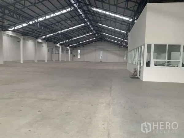 Warehouse for rent in Phra Pradaeng, Samut Prakan - Open‑plan warehouse interior with steel truss roof, polished concrete floor and a glass‑partitioned office block.