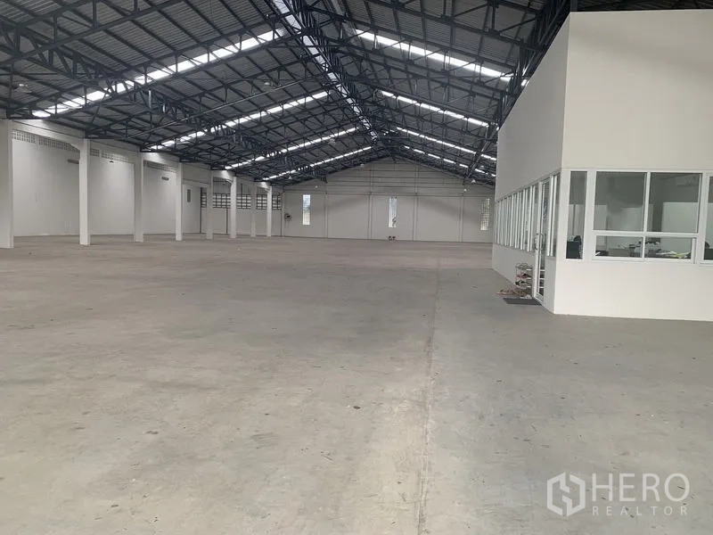 Warehouse for rent in Phra Pradaeng, Samut Prakan - Open‑plan warehouse interior with steel truss roof, polished concrete floor and a glass‑partitioned office block.