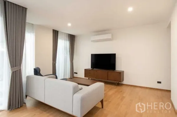 Condominium for rent in Phra Khanong, Bangkok - Bright living room with grey sofa, TV console, wood flooring and wall-mounted air conditioner.