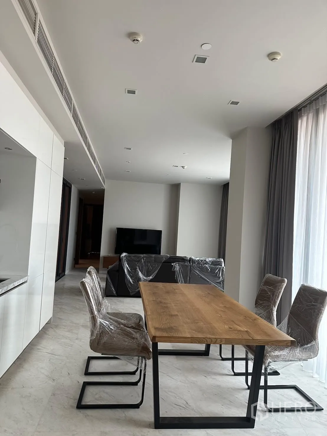 Condominium for rent or sale in Watthana, Bangkok - Dining area with wooden table, four upholstered chairs, and large windows.