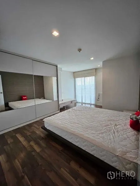 Condominium for sale in Watthana, Bangkok - Primary bedroom with large mirrored wardrobe, bed, and floor-to-ceiling window.