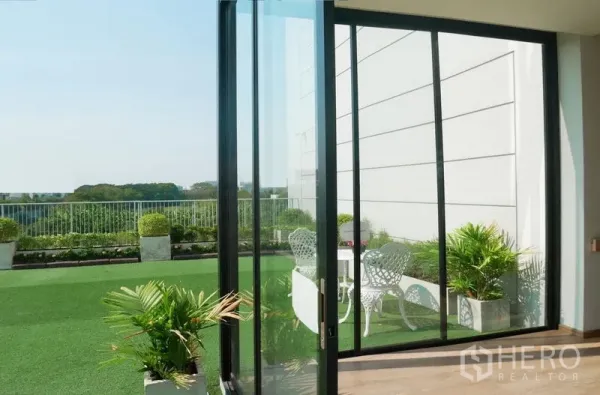 พื้นที่ขายปลีก ให้เช่าในBang Kapi, Bangkok - ประตูบานเลื่อนกระจกเปิดสู่ดาดฟ้าปูหญ้าเทียม มีต้นไม้กระถางและชุดโต๊ะเก้าอี้สีขาว