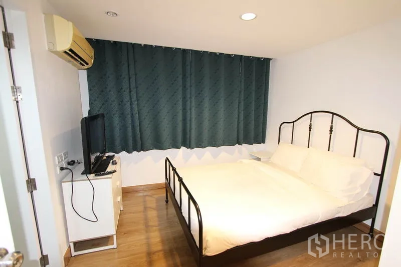 Condominium for rent or sale in Wang Thonglang, Bangkok - Master bedroom with metal-frame bed, air conditioning, TV stand, and blackout curtains.