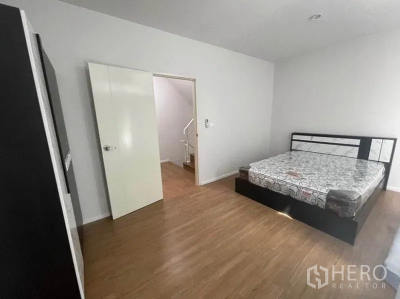 Townhouse for rent in Phasi Charoen, Bangkok - Large bedroom with bed, wood floors, open door to landing and wardrobe.