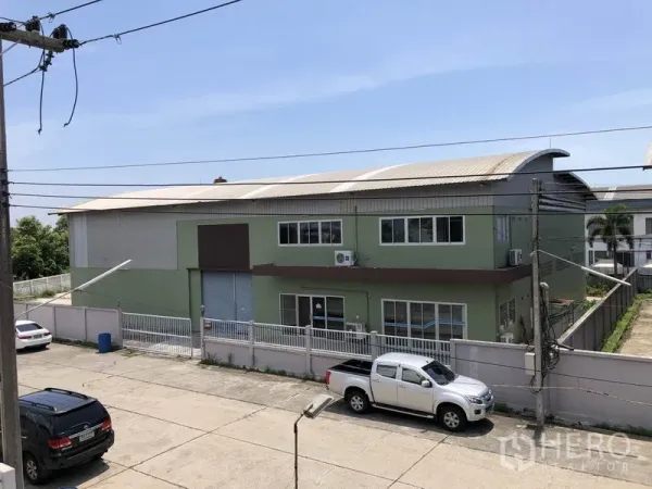 工厂 出租在Pathum Thani - 街景角度可见带围栏和卷闸门的绿色两层工厂外观