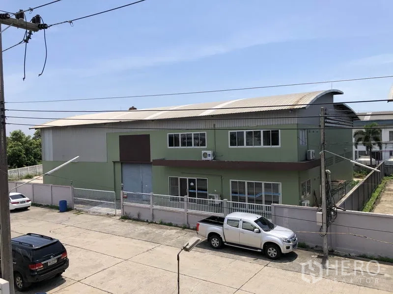 工厂 出租在Pathum Thani - 街景角度可见带围栏和卷闸门的绿色两层工厂外观