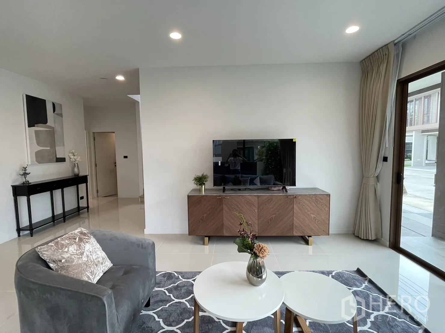Detached House for rent in Bang Kapi, Bangkok - Living area with TV console, lounge chair, and coffee tables near sliding doors.