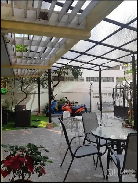 บ้าน ให้เช่าในWatthana, Bangkok - เฉลียงมีหลังคาใส โต๊ะนั่งเล่นกลางแจ้ง และมอเตอร์ไซค์จอดข้างสนามหญ้า