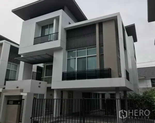 Detached House for sale in Suan Luang, Bangkok - Angle view of modern white detached house with tall windows, balcony and front fence.
