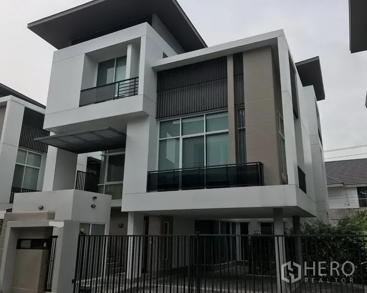 Detached House for sale in Suan Luang, Bangkok - Angle view of modern white detached house with tall windows, balcony and front fence.