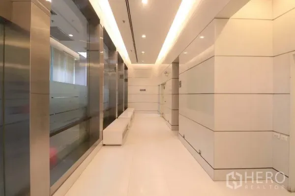 办公空间 出租在Bang Rak, Bangkok - 现代电梯大堂，玻璃墙与不锈钢装饰并设有内置座椅。
