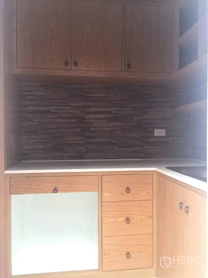 ทาวน์เฮาส์ ให้เช่าหรือขายในLat Phrao, Bangkok - ครัวรูปตัวแอล ตู้ไม้ ผนังกันเปื้อนลายหิน และท็อปสีขาว