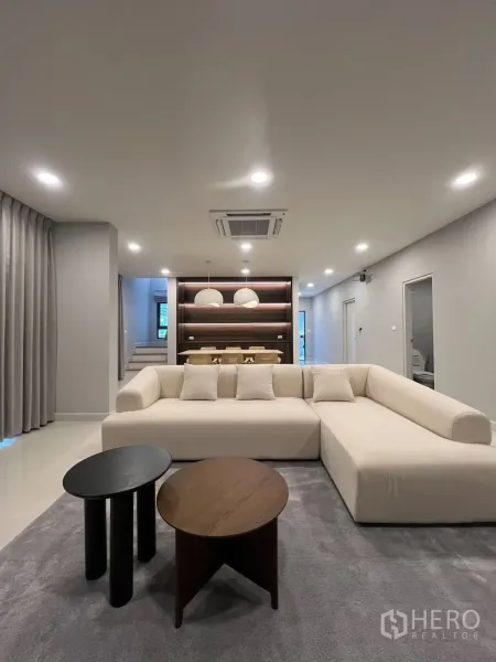 Detached House for rent in Bang Phli, Samut Prakan - Open-plan lounge facing built-in wood shelving and a dining area with pendant lights.