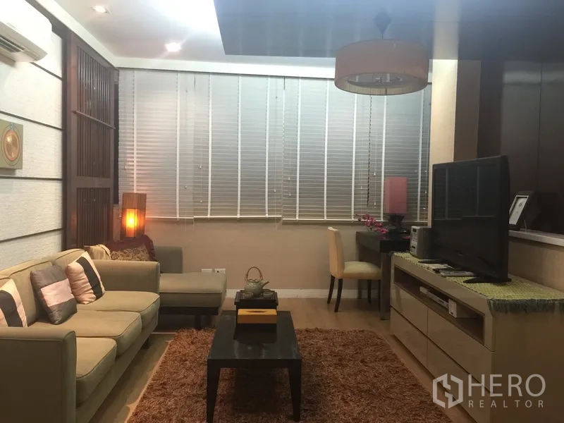 Condominium for rent or sale in Sathon, Bangkok - Modern living room with L-shaped sofa, TV console, desk and large window blinds.