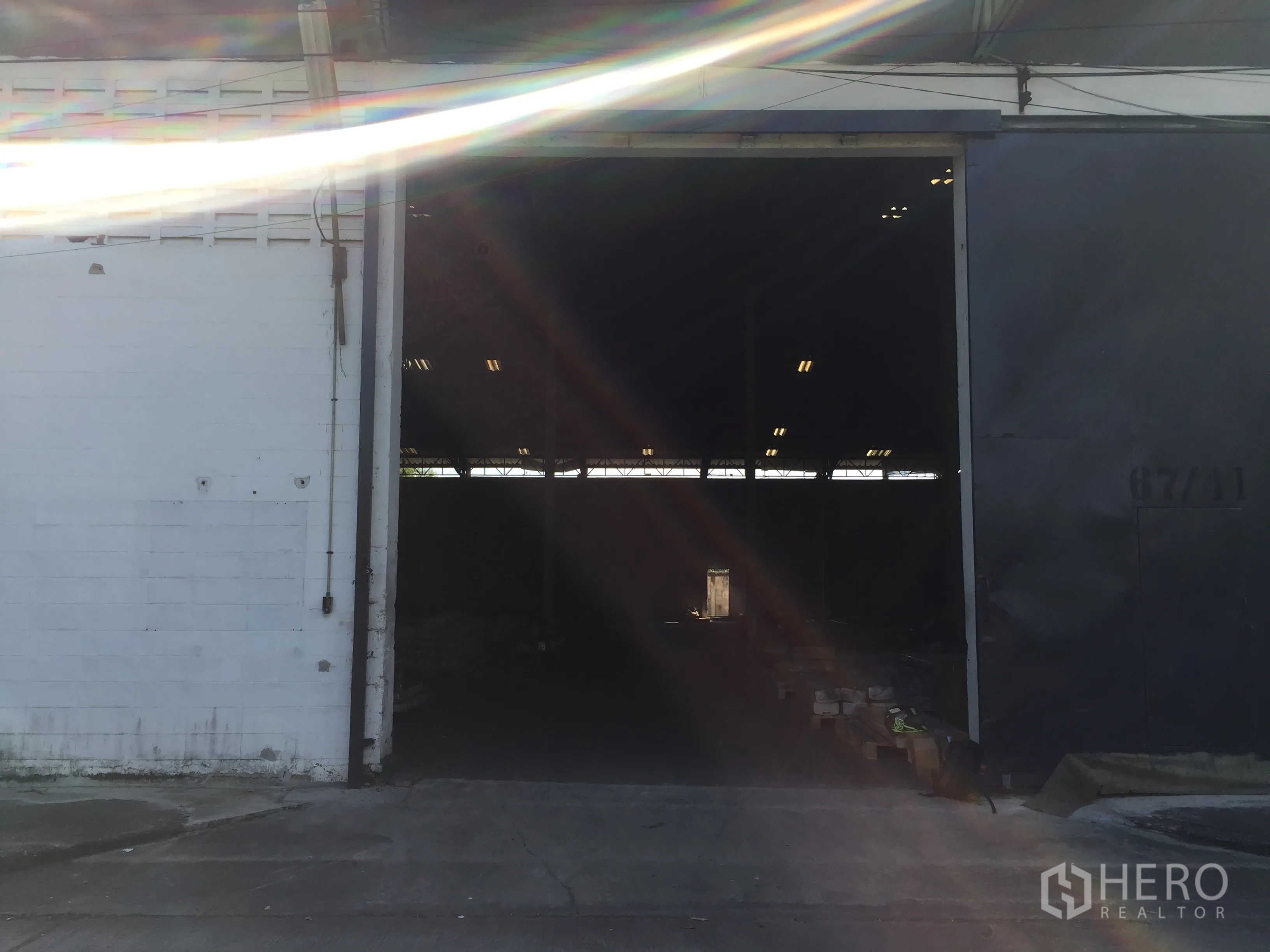 工厂 出租在Pathum Thani - 大型金属推拉门开启，阳光照入昏暗的仓库内部。