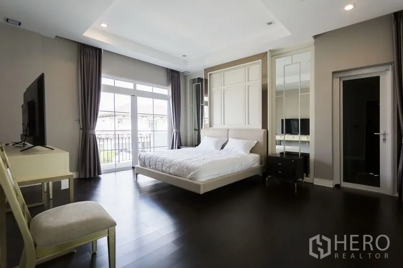 独立式住宅 出租在Mueang Samut Prakan, Samut Prakan - 主卧带阳台，深色木地板与衣柜，采光良好。