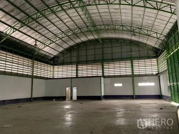 Warehouse for rent in Lam Luk Ka, Pathum Thani - Spacious warehouse interior with high arched metal roof, green steel trusses, louvered vents and concrete floor.