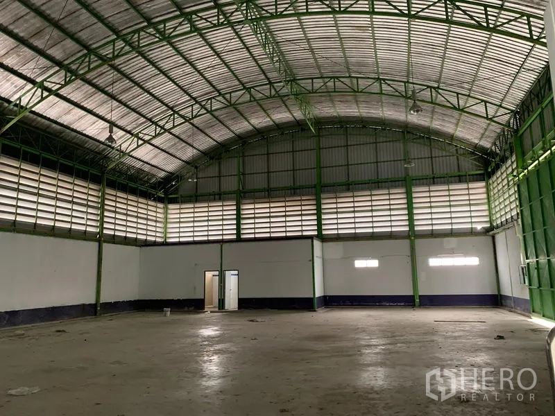 Warehouse for rent in Lam Luk Ka, Pathum Thani - Spacious warehouse interior with high arched metal roof, green steel trusses, louvered vents and concrete floor.