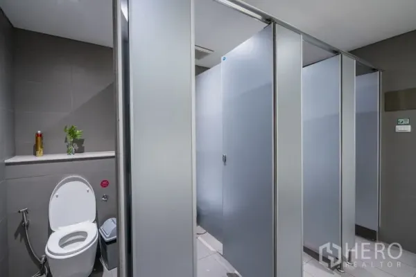 สำนักงาน ให้เช่า - แถวห้องสุขาพร้อมฉากกั้นสีเทาและโถส้วมแบบตะวันตกในห้องมุม