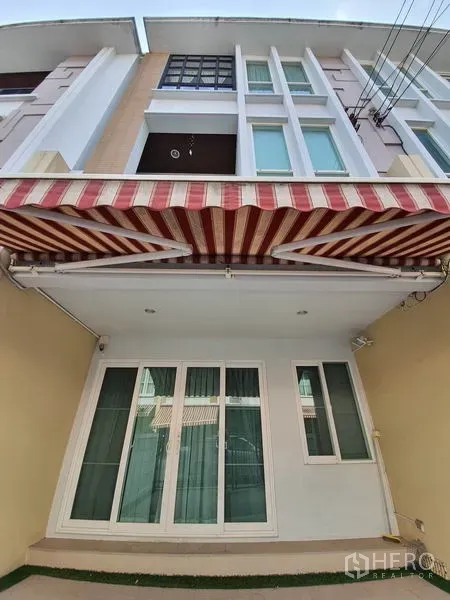Townhouse for rent in Wang Thonglang, Bangkok - Three-story townhouse facade with striped retractable awning and sliding glass doors.