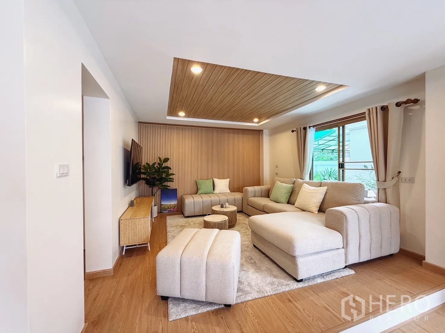 独立式住宅 出售在Suan Luang, Bangkok - 明亮客厅，米色沙发、木质吊顶与壁挂电视。