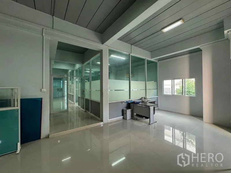 Warehouse for rent or sale in Chon Buri - Open-plan office area with frosted glass partitions, windows and a work desk.