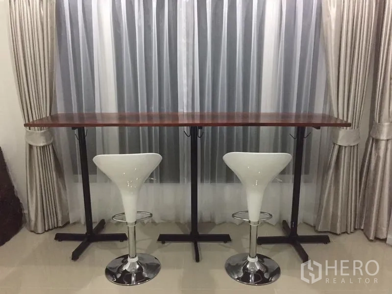 Detached House for sale in Prawet, Bangkok - Dining bar with wooden countertop and two white bar stools beside curtained window.