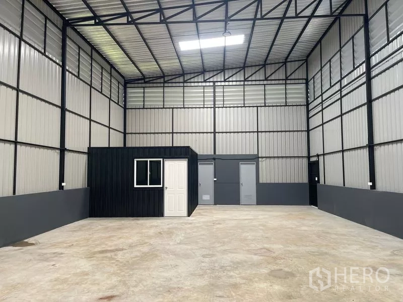 Warehouse for rent in Wang Thonglang, Bangkok - Spacious high-ceiling warehouse interior with steel trusses, skylight panel, and a built-in office room.