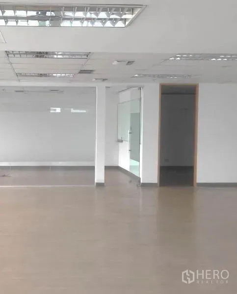 Office Space for rent in Bang Rak, Bangkok - Empty office interior with suspended fluorescent lighting, glass door and access to a utility/pantry area.