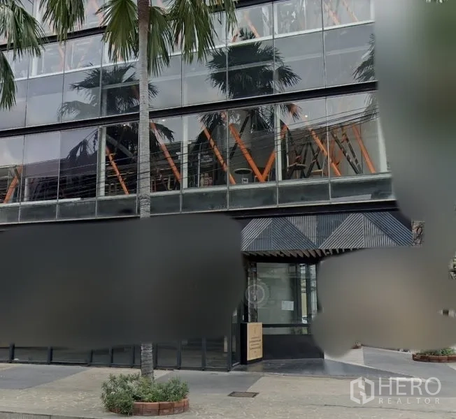 零售空间 出租在Watthana, Bangkok - 带雨棚的宽阔玻璃门面，镜面窗与棕榈树步道的商业建筑入口。