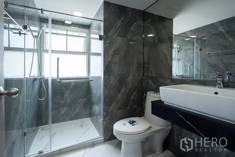 Apartment for rent - Second bathroom with dark stone tiles, glass shower and wide mirror.