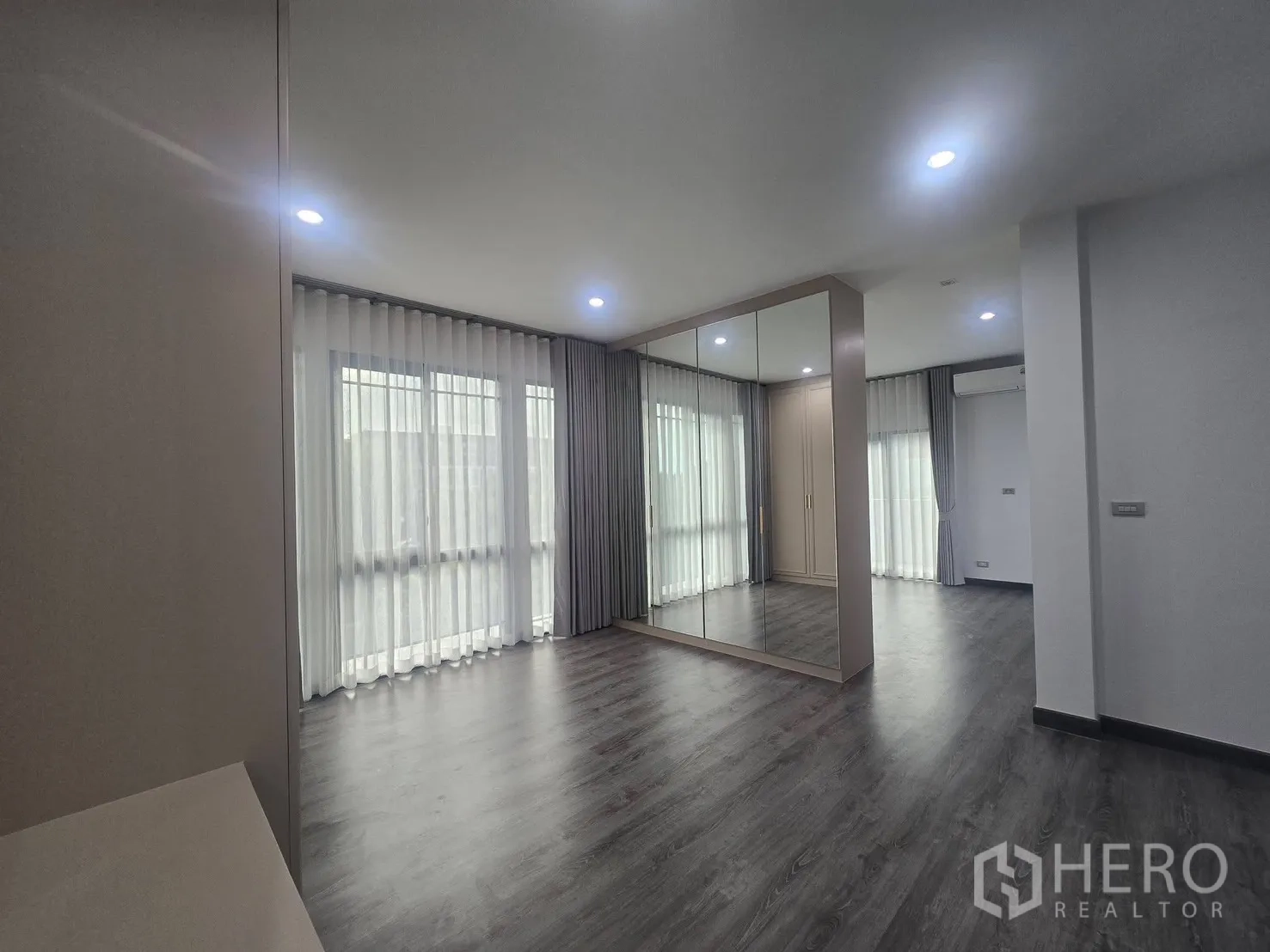 Semi-detached House for rent in Suan Luang, Bangkok - Bedroom area with mirrored wall wardrobe, grey wood floors and soft lighting.