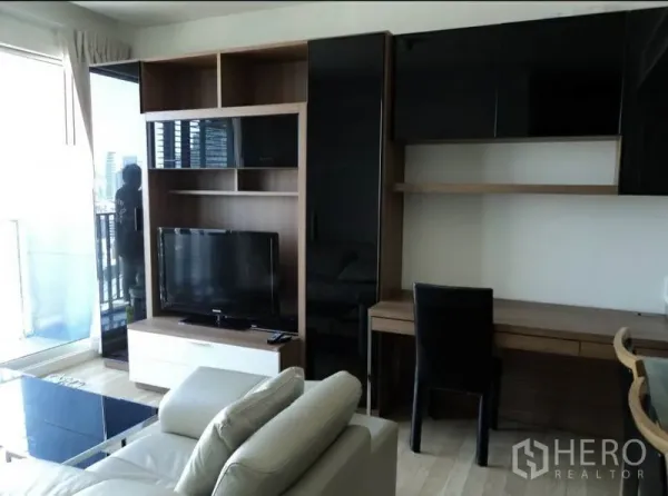 คอนโด ให้เช่าในKhlong Toei, Bangkok - มุมนั่งเล่นมีชั้นวางทีวี ตู้บิลท์อิน โต๊ะทำงาน และโซฟาหนังข้างระเบียง