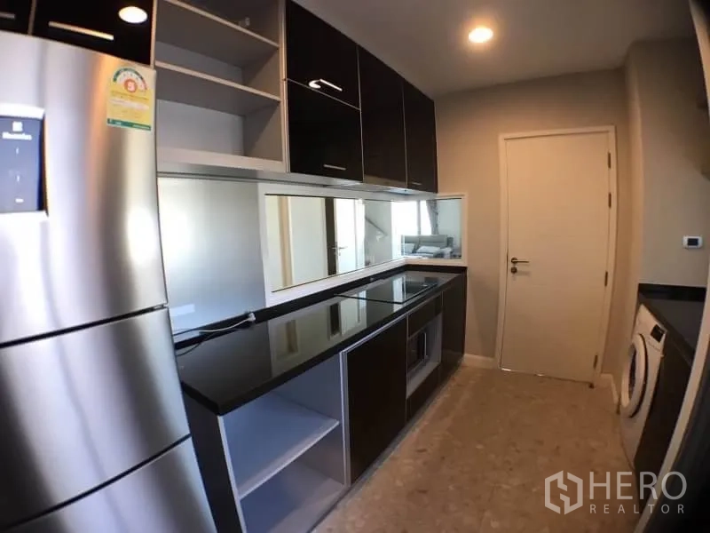 Condominium for rent in Khlong Toei, Bangkok - Galley kitchen showing ample storage, appliances and a laundry corner.