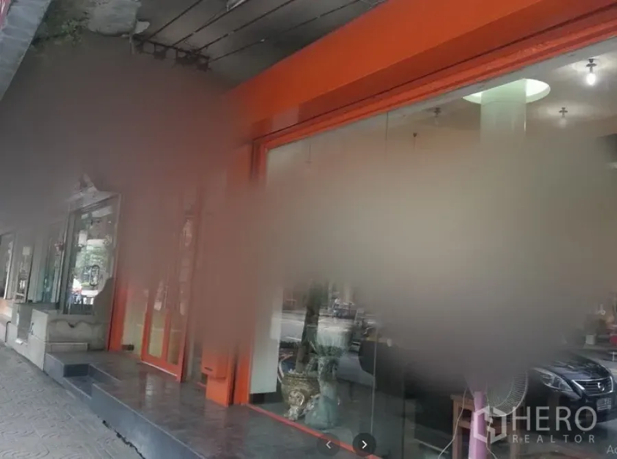 Shophouse for rent in Watthana, Bangkok - Street-level shophouse exterior with orange-framed glass storefront, steps, and a covered sidewalk in an urban area.
