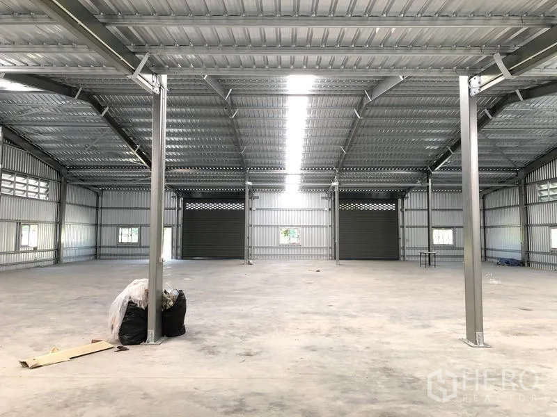 Warehouse for rent in Pak Kret, Nonthaburi - Central aisle facing three roller doors beneath bright roof skylight strip.